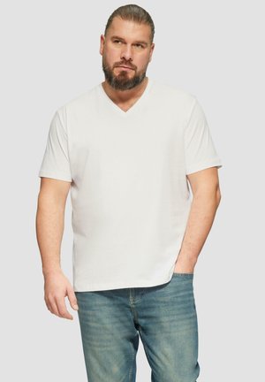 Biała bawełniana koszulka V-neck z krótkim rękawem, luźny krój i gładka faktura; w połączeniu z jasnoniebieskimi dżinsami.
