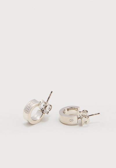 Ζεύγος ασημένιων σκουλαρικιών κρίκου με πίσω κούμπωμα, το ένα με χαραγμένους αριθμούς και γράμματα στην εξωτερική άκρη, σε λευκό φόντο.