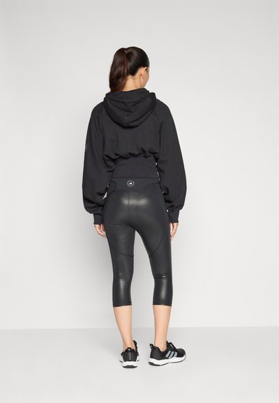 Fekete kapucnis pulcsi puffos ujjal, fényes fekete capri leggings-szel párosítva. A lábbeli fekete, fehér részletekkel.