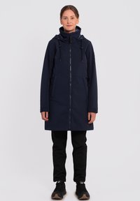 Veste imperméable bleu marine avec capuche, cordons de serrage réglables, fermeture éclair et poches latérales. Texture lisse, design jusqu'aux genoux.