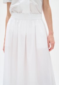 White, mid-length skirt with an elastic waistband, featuring a smooth, lightweight fabric and soft pleats for a relaxed silhouette.