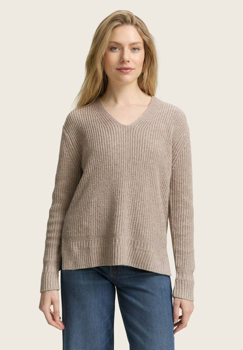 Light beige knitted sweater with a V-neck, ribbed cuffs and hem, featuring a textured pattern and a relaxed fit. Paired with blue jeans.