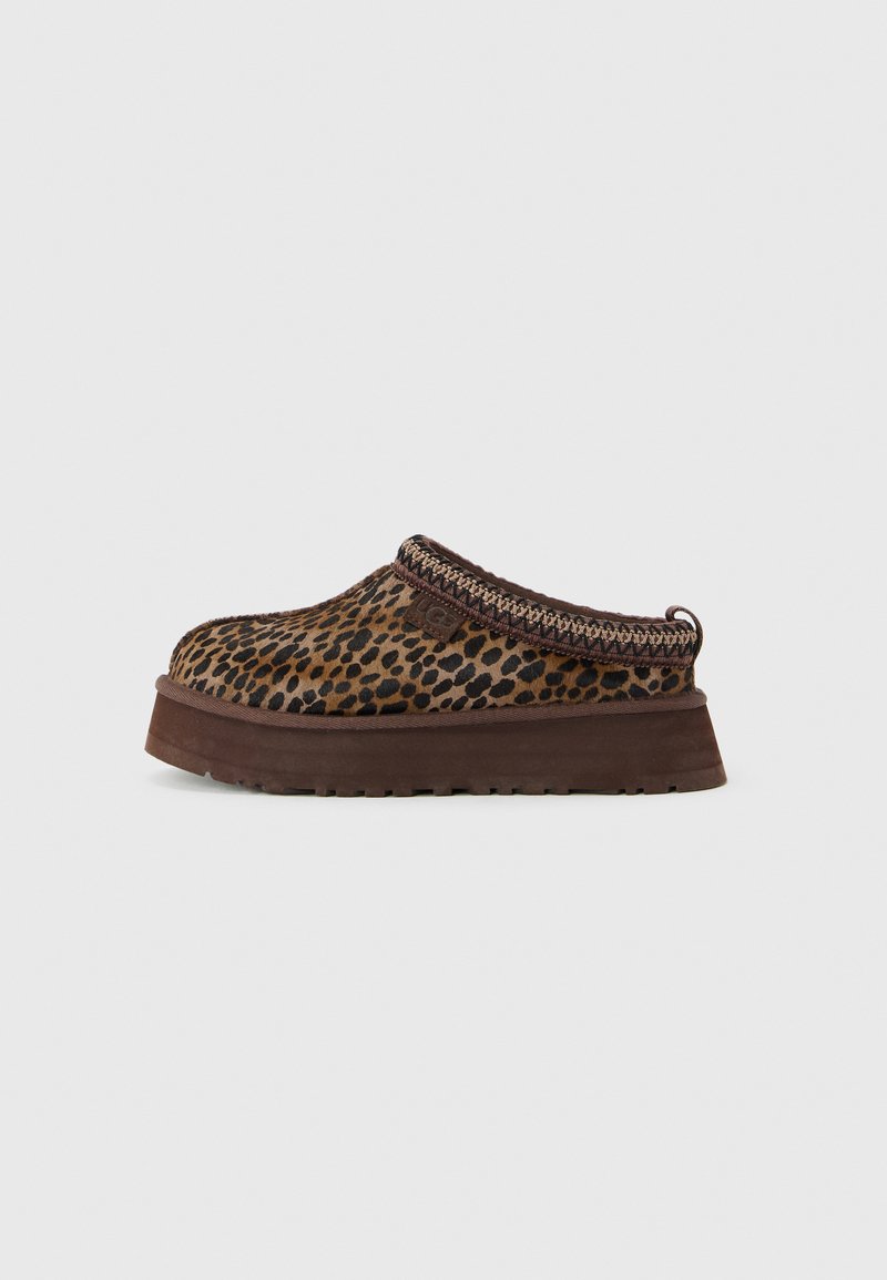 Bruine instapper met een bovenwerk van leoplatchterstof en een dikke zool, decoratieve stiksels bij de kraag en een merklabel aan de zijkant.