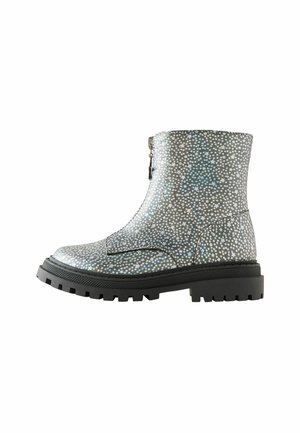Botte haute jusqu'à la cheville avec une semelle épaisse noire, recouverte de motifs étoilés argentés et holographiques, dotée d'une fermeture éclair à l'avant.