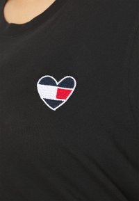 Sort bomulds T-shirt med et hjerteformet broderet logo, der inkluderer marineblå, rød og hvide sektioner. Rund halsudskæring, design med korte ærmer.