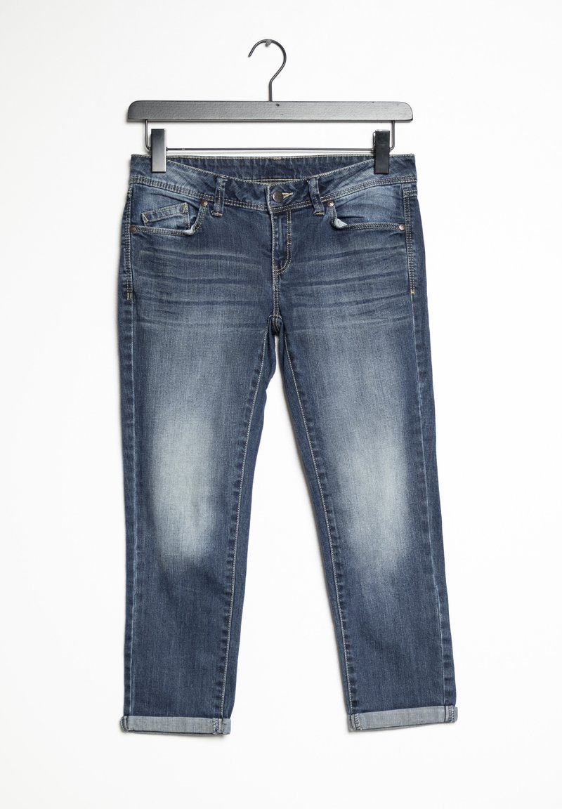 Pantalones vaqueros de denim azul oscuro colgados en una percha, con un lavado desgastado, diseño de cinco bolsillos, cremallera frontal y puños enrollados en los tobillos.