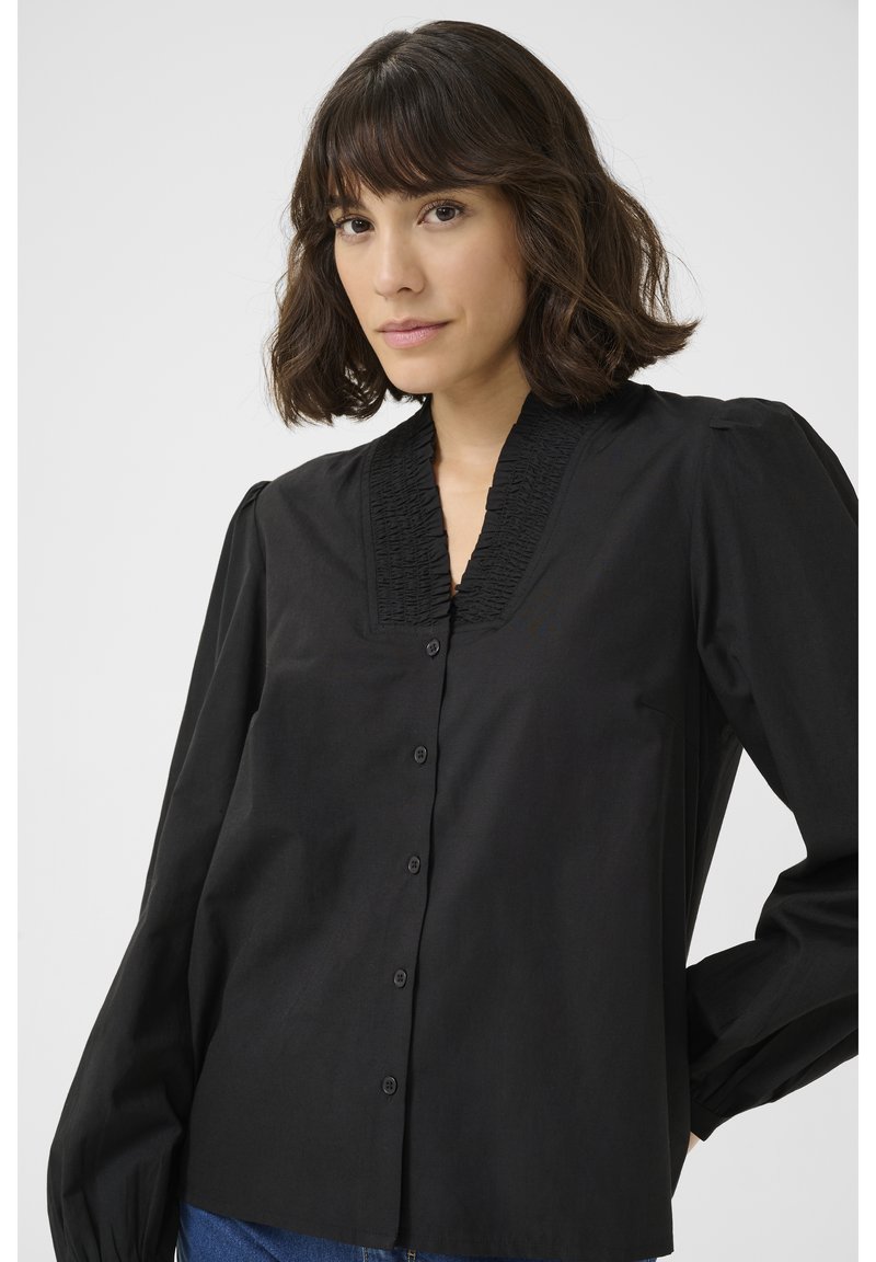 Blouse noire avec un col plissé texturé, des manches longues et une fermeture à boutons sur le devant. Fabriquée en tissu lisse, elle présente une coupe décontractée.