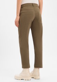 Pantalon fuselé vert olive en mélange de coton, avec deux poches arrière. Porté avec des bottines beiges, présentant un design simple.