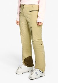 Light beige ski pants with zippered pockets, a brown accent at the ankle, made from waterproof material, featuring a sleek, tapered design.