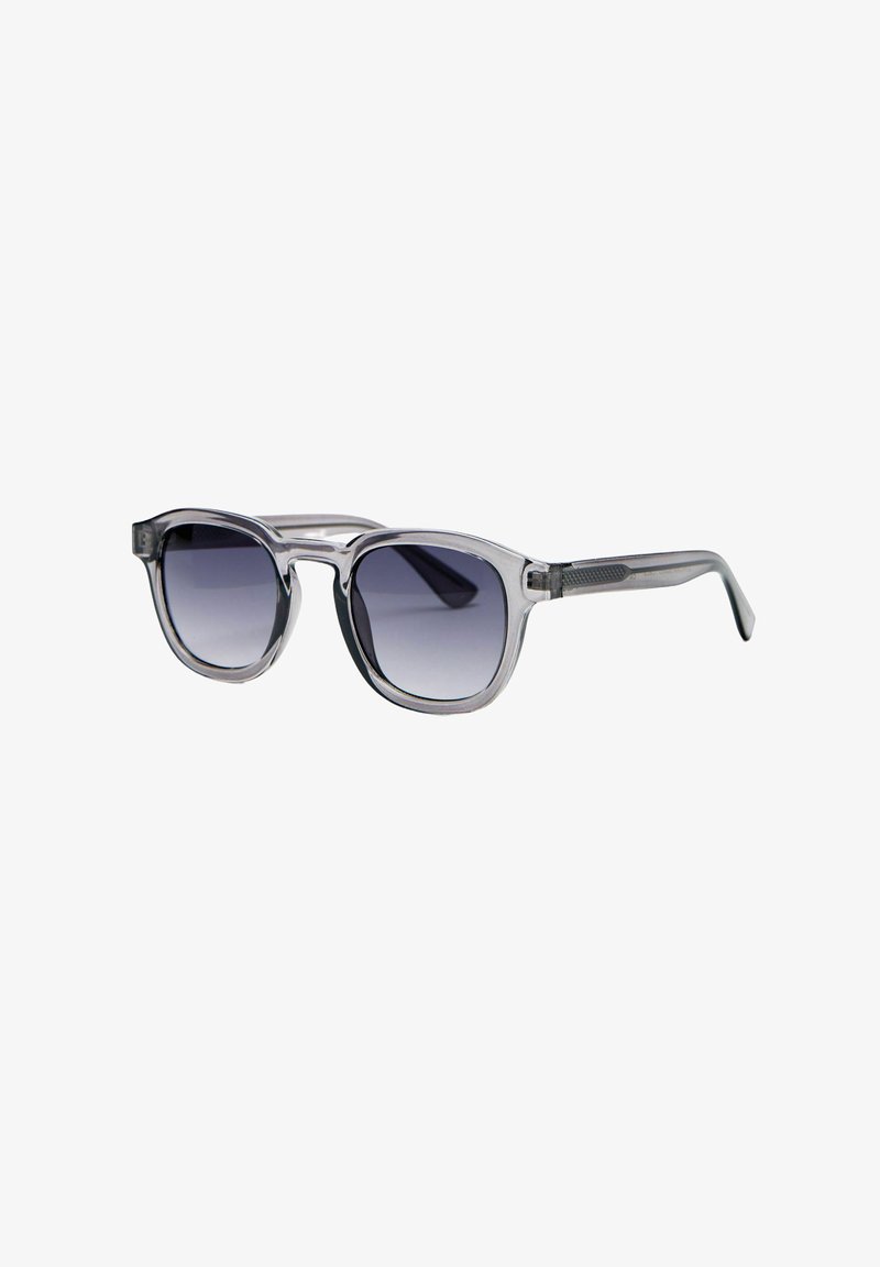Lunettes de soleil à monture en plastique gris transparent avec verres carrés dégradés foncés et branches droites légèrement inclinées vers l'extérieur.
