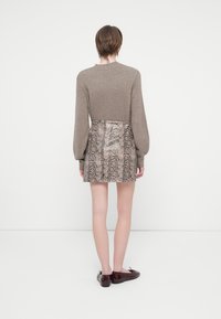 Maglione lavorato a maglia marrone con maniche a sbuffo, abbinato a una mini gonna aderente con stampa pitone lucida. La modella indossa scarpe di un profondo bordeaux.