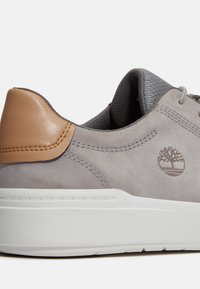 Grå mockaskinnssneaker med en tan läderklack, vit gummisula och stygninslag. Har Tree-logotypen präglad på sidan.