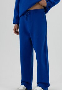 Blauwe sweatpants gemaakt van zachte stof, met een losse pasvorm, elastische tailleband met trekkoord en zijzakken. Platte naden accentueren het ontwerp.