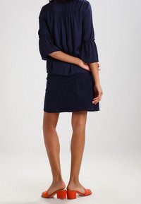 Marinblus med utsvängda ärmar, kombinerad med en marin kjol. Modellen bär orange klacksandaler. Slät tyg och avslappnad passform.