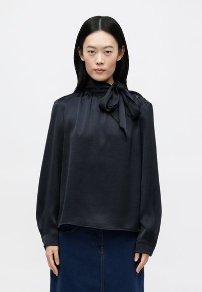 Blusa azul oscuro en tela lisa, con cuello alto y detalle de lazo. Mangas largas con botones en los puños.