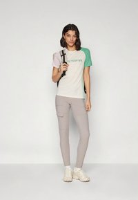 Lühikeste varrukatega mitmevärviline T-särk roheliste, roosade ja valgete osadega; sobivad heledates hallides pükstes taskutega; vabaaja jalanõud.