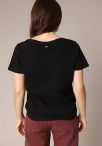 Black short-sleeved t-shirt with a round neckline, featuring a small gold accent on the back. Fabric appears soft and lightweight.