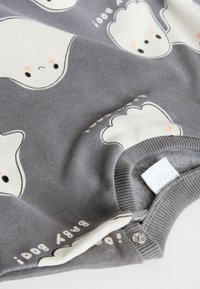 Hall hallist puuvillast beebiriietus valgete kummitusmustritega, mis on varustatud presskinnitustega ja pehme tekstuuriga. "Baby Boo!" on trükitud äärele.