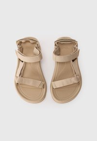 Beige open-toe sandals with adjustable fabric straps over toes and around ankles, flat textured soles, laid side by side on white background.