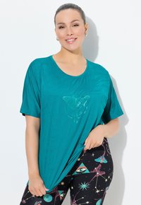 Camiseta color teal de tela ligera con cuello redondo y mangas cortas. Presenta un diseño sutil de mariposa en la parte frontal.