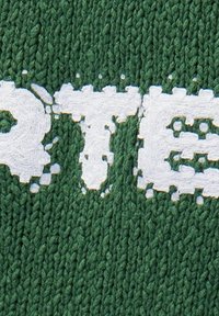 Tessuto di maglia verde con una superficie texture, caratterizzato da lettere bianche che appaiono leggermente usurate o irregolari nella forma.