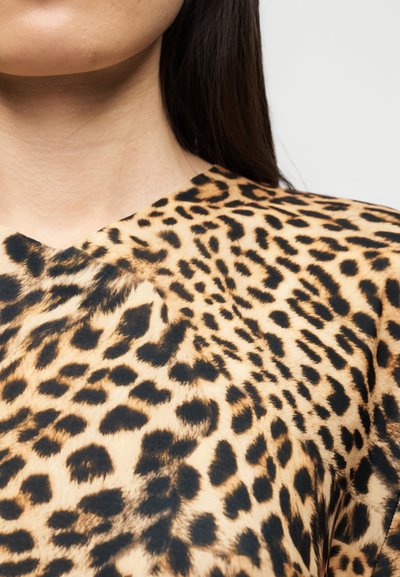 Τοπ με λεοπάρ σχέδιο που διαθέτει V-λαιμόκοψη, κατασκευασμένο από απαλό ύφασμα με συνδυασμό καφέ και μαύρων κηλίδων, αναδεικνύοντας ένα τολμηρό μοτίβο.
