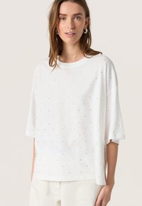 Hvid bomulds T-shirt med korte ærmer og en afslappet pasform, der har små, spredte metalliske detaljer på forsiden.