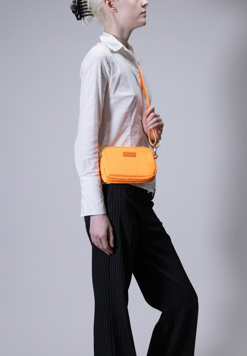Borsa a tracolla arancione realizzata in un materiale liscio, dotata di chiusura con zip, tracolla regolabile e logo in evidenza sulla parte anteriore.