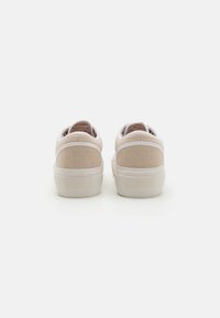 Baskets en toile beige avec des accents blancs, présentant un dos texturé, un col rembourré et le logo Roxy sur le talon. Design simple et discret.