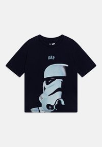 Juodas medvilninis marškinėliai su Stormtrooper šalmą vaizduojančia grafika, viršuje su "GAP" logotipo. Trumpomis rankovėmis ir laisvu kirpimu.