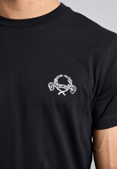 Svart bomull T-skjorte med en hvit brodert logo med en laurbærkrans og krysset objekter på venstre bryst. Korte ermer, rund hals.