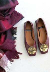 Ballerine in pelle bordeaux con punta arrotondata e accentuazione metallica dorata. Accompagnate da una sciarpa a quadri bordeaux e nera con bordi frangiati.