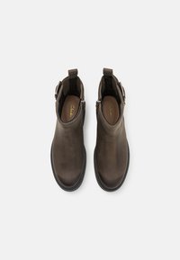 Botas de tobillo de cuero marrón con una textura suave, punta redonda, tacón bajo y cierre de cremallera. Incluyen una lengüeta para facilitar el calzado.