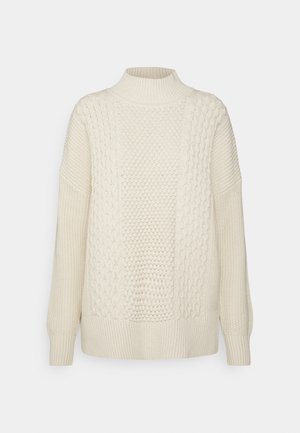 Pull en tricot couleur crème avec un col montant, présentant des panneaux texturés et des manches à poignet côtelé. Tissu doux et épais avec une coupe décontractée.