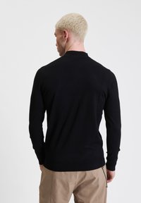 Maglione nero a maniche lunghe con design aderente, texture liscia e scollatura a girocollo, visto da dietro.