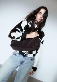 Kurtka z futra w czarno-białą łatę, w połączeniu z jasnoniebieskimi dżinsami w stylu vintage. Ciemnobrązowa torebka z kordurowej tkaniny o żebrowanej fakturze.
