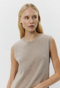 Beige ærmeløs strik top med rund hals, der har en glat tekstur og subtile farvevariationer, der fremhæver det åndbare materiale.