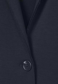 Donkerblauwe blazer stof met een enkele zwarte viergaatjesknop bevestigd op de voornaad nabij de revers.