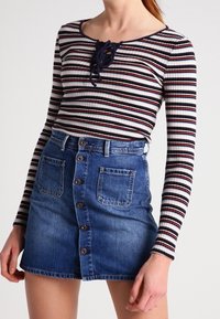 Randig långärmad topp med snörning i halsen, matchad med en jeanskjol med knappstängning fram och två framfickor.