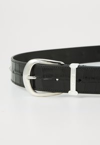 Cureau din piele cu embossing crocodil negru, cu o cataramă metalică argintie și detalii decorative. Are cusături vizibile și gauri ajustabile.