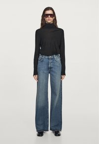 Czarna bluzka z golfem, w połączeniu z szerokimi niebieskimi dżinsami. Dżinsy mają wyblakły odcień i wysoką talię. Duże okulary przeciwsłoneczne dopełniają stylizację.