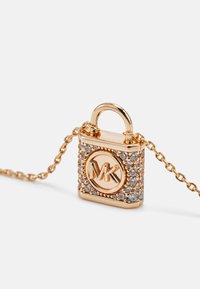 Colgante en forma de candado dorado con cristales transparentes y el logo "MK", unido a una cadena dorada sobre un fondo blanco.