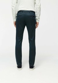 Dunkelgrüne, schmal geschnittene Hose mit zwei Gesäßtaschen, glatter Stoffoberfläche und sicherem Bund, getragen mit weißen und schwarzen Sneakers.