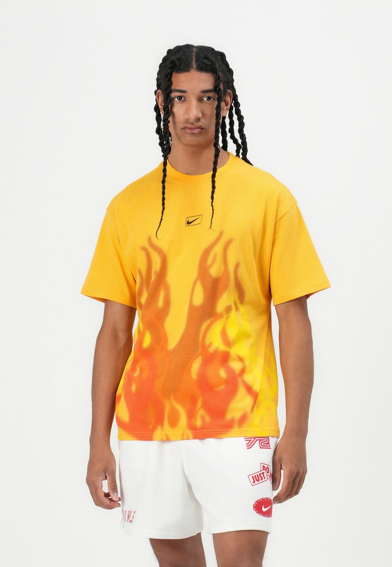 Tricou galben cu un design de flacără portocalie, cu mâneci scurte și gât rotund. Logo-ul Nike în centru, deasupra flăcărilor.