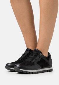 Czarne sneakersy z połączenia gładkiej skóry i teksturowanego zamszu. Design obejmuje sznurowane zapięcie z przodu, zamek po bokach oraz wyściełaną gumową podeszwę.