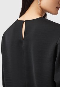 Svart klänning med en nyckelhålsdetalj på ryggen; slätt, glänsande tyg med en lätt lyster; minimalistisk design och avslappnad passform, ingen synlig hårdvara.