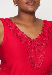 Top vermelho sem mangas com um decote em V ricamente bordado, adornado com padrões florais e detalhes intrincados, feito de um tecido suave e macio.