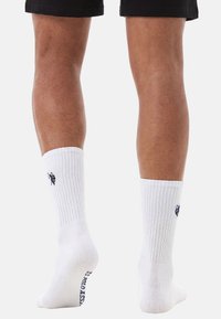 Legs wearing white ribbed crew socks with a small navy logo on the side and black shorts against a plain background.