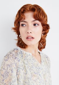 Blusa a fantasia floreale con un tessuto leggero e trasparente in colori pastello, caratterizzata da una scollatura a V e leggere maniche a sbuffo.