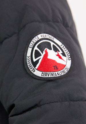 Zwarte pufferjack met een mouw die een ronde geborduurde patch heeft. De patch heeft een bergontwerp met rode accenten, tekst en een decoratieve rand.